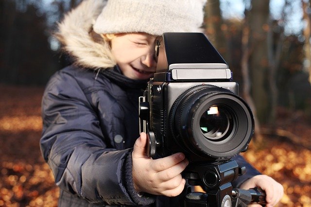 young child looking through large camera in a woods