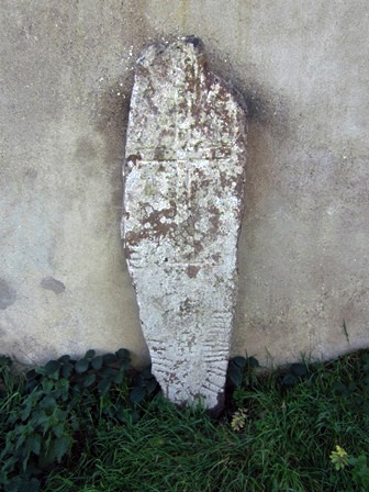 small upright ogham stone leaning against a wall