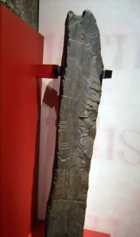 large flat ogham stone help to a red panel on a wall